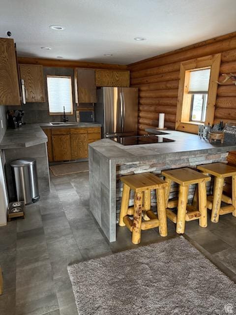 kitchen featuring brown cabinetry, freestanding refrigerator, log walls, black electric cooktop, and a sink