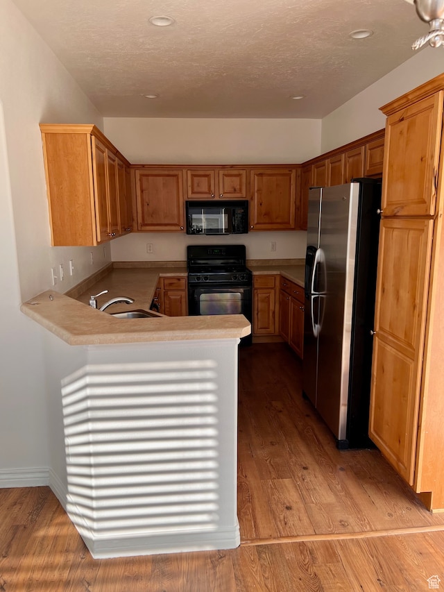 3119 N Sage Loop Unit F3, Lehi, UT 84043 - kitchen with kitchen peninsula, a textured ceiling, light wood-type flooring, black appliances, and sink