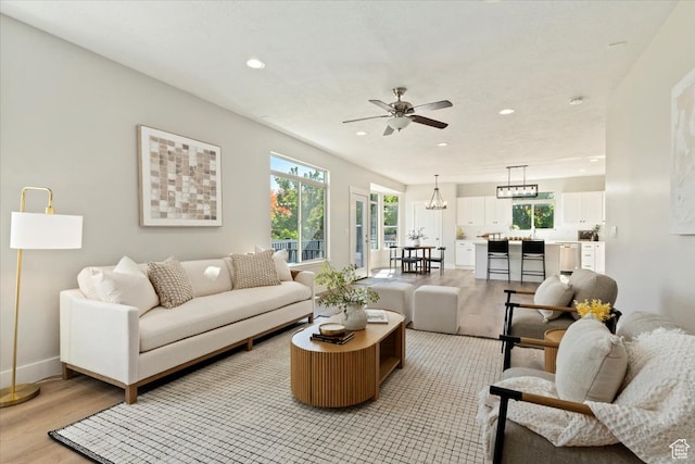 living room featuring ceiling fan with notable chandelier and light hardwood / wood-style floors