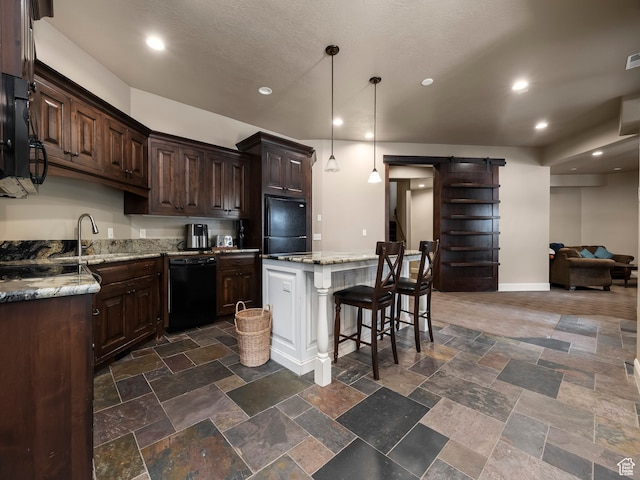 kitchen with light stone countertops, pendant lighting, black appliances, a kitchen island, and a barn door