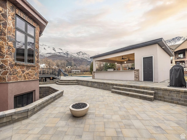 view of patio with ceiling fan, an outdoor fireplace, and a mountain view