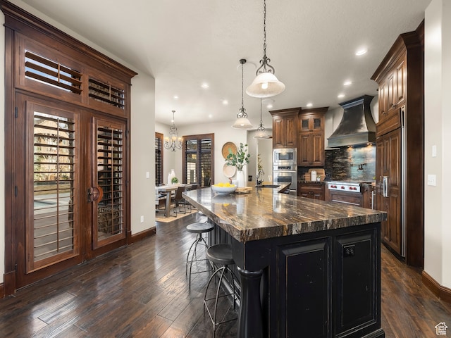 kitchen with stainless steel appliances, premium range hood, hanging light fixtures, a large island, and a breakfast bar