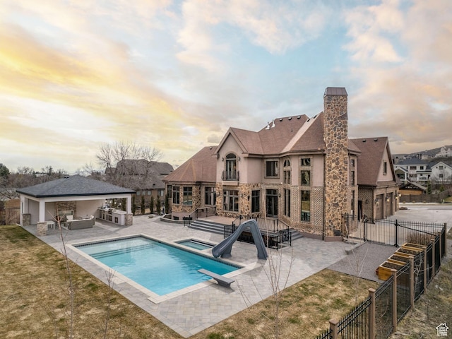 pool at dusk with a jacuzzi, a water slide, a diving board, area for grilling, and a patio