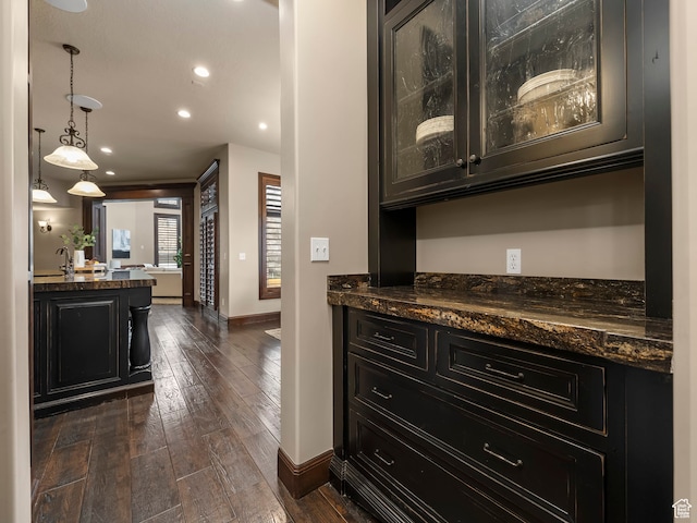 bar featuring dark hardwood / wood-style flooring, pendant lighting, and dark stone counters
