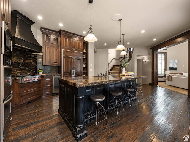 kitchen with tasteful backsplash, pendant lighting, custom exhaust hood, appliances with stainless steel finishes, and a large island