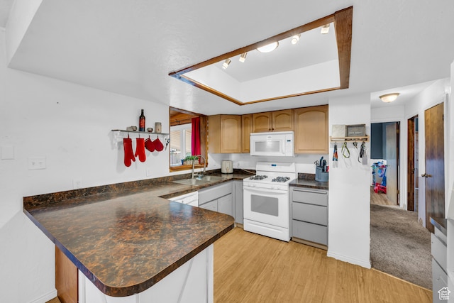 kitchen featuring white appliances, sink, light wood-type flooring, a raised ceiling, and kitchen peninsula