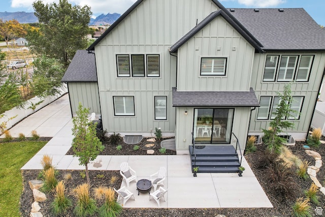 rear view of house featuring board and batten siding, a patio, roof with shingles, and a mountain view