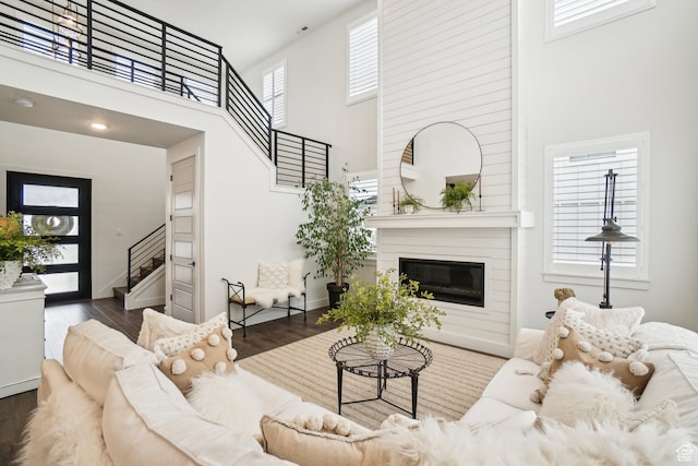 living area featuring wood finished floors, a high ceiling, baseboards, a large fireplace, and stairs