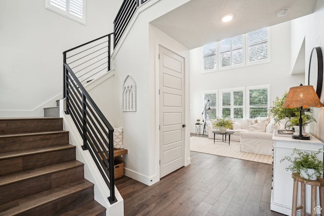 stairway featuring baseboards, hardwood / wood-style floors, recessed lighting, and a towering ceiling