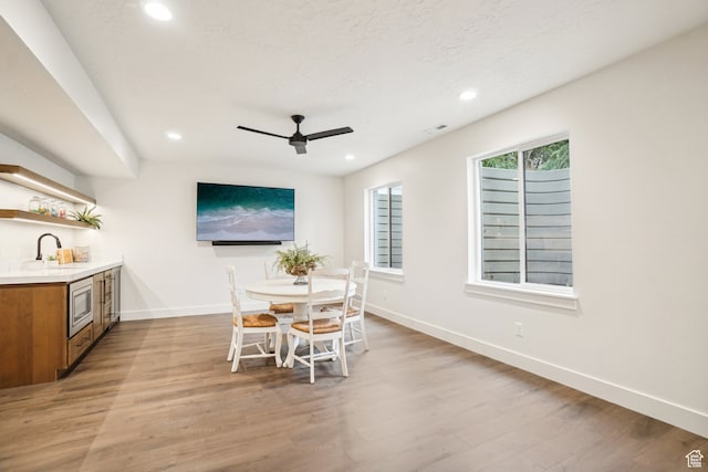 dining area featuring indoor wet bar, light wood-type flooring, baseboards, ceiling fan, and recessed lighting