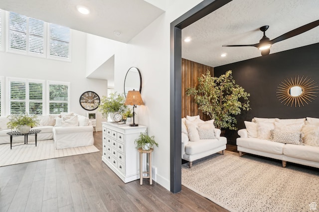 living area with a healthy amount of sunlight, an accent wall, ceiling fan, dark wood-style flooring, and a high ceiling