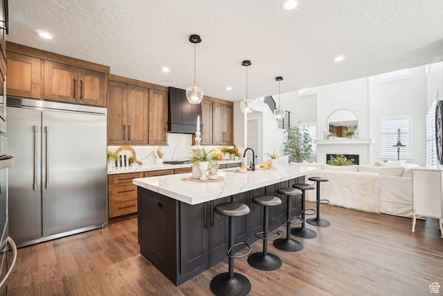kitchen with brown cabinetry, open floor plan, premium range hood, wood finished floors, and appliances with stainless steel finishes