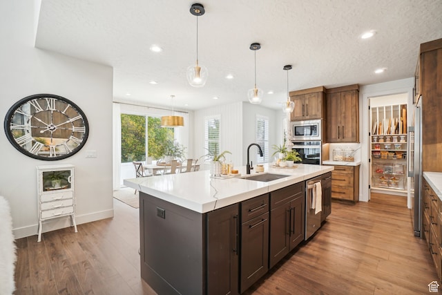 kitchen with a sink, stainless steel appliances, wood finished floors, recessed lighting, and light countertops