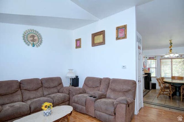 living room with a chandelier, lofted ceiling, and light wood-type flooring