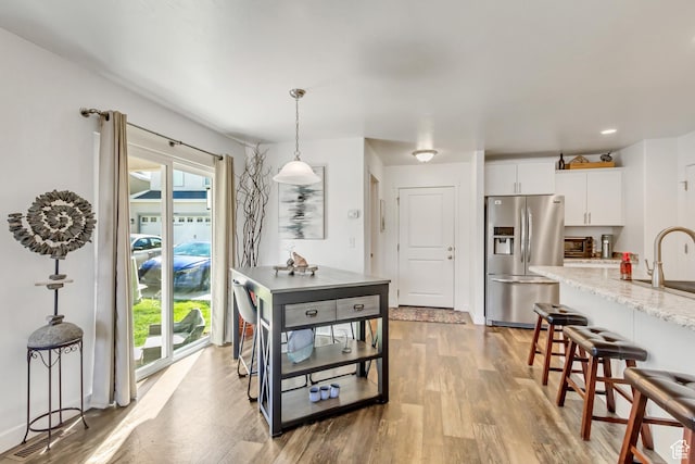 kitchen with a kitchen bar, hanging light fixtures, light wood finished floors, stainless steel fridge, and white cabinetry