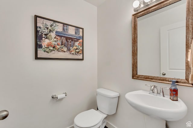 half bathroom featuring baseboards, a sink, and toilet