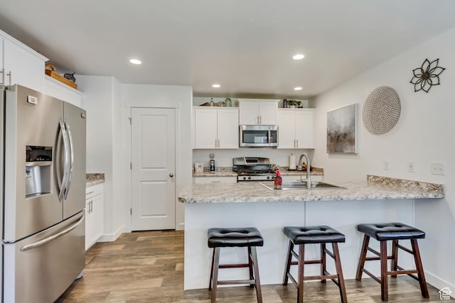 kitchen with a sink, appliances with stainless steel finishes, a peninsula, and wood finished floors