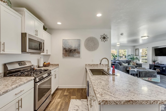 kitchen with a sink, a peninsula, open floor plan, stainless steel appliances, and dark wood-type flooring