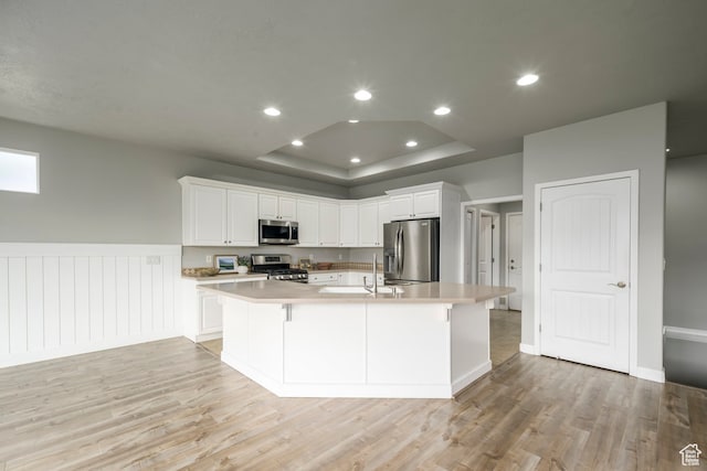 kitchen with a tray ceiling, stainless steel appliances, white cabinets, and light wood finished floors