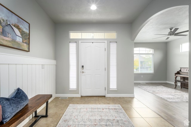 tiled entryway featuring arched walkways, baseboards, a textured ceiling, and ceiling fan