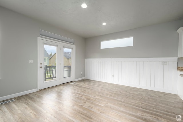 empty room with a textured ceiling, visible vents, light wood finished floors, and wainscoting