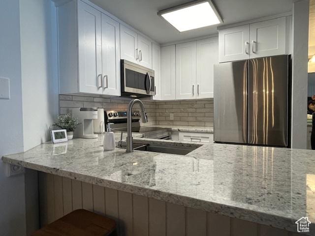 385 S Vasels Rd Unit 21, Brian Head, UT 84719 - kitchen featuring appliances with stainless steel finishes, a peninsula, light stone counters, backsplash, and white cabinets