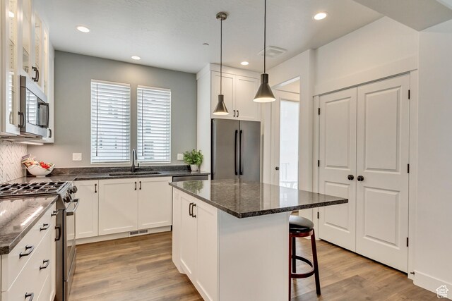 11211 S Clear Blue Dr, South Jordan, UT 84009 - kitchen with stainless steel appliances, a sink, white cabinets, a kitchen breakfast bar, and light wood finished floors