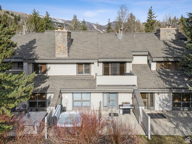 back of property featuring a shingled roof, a patio area, a mountain view, and a chimney