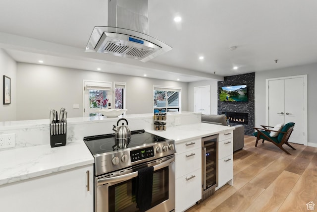 kitchen with wine cooler, island exhaust hood, white cabinetry, and stainless steel range with electric stovetop