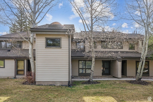 back of house featuring a shingled roof, a yard, and a balcony