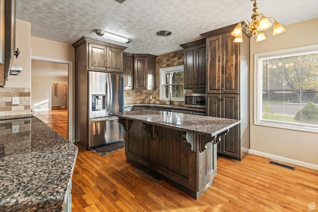 455 N 500 W, Richfield, UT 84701 - kitchen featuring appliances with stainless steel finishes, dark brown cabinets, tasteful backsplash, a kitchen bar, and light wood-style flooring