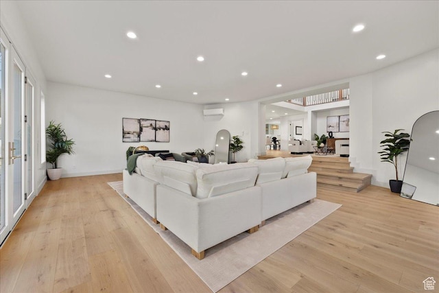 living area with a wall mounted AC, light wood-style floors, recessed lighting, and arched walkways