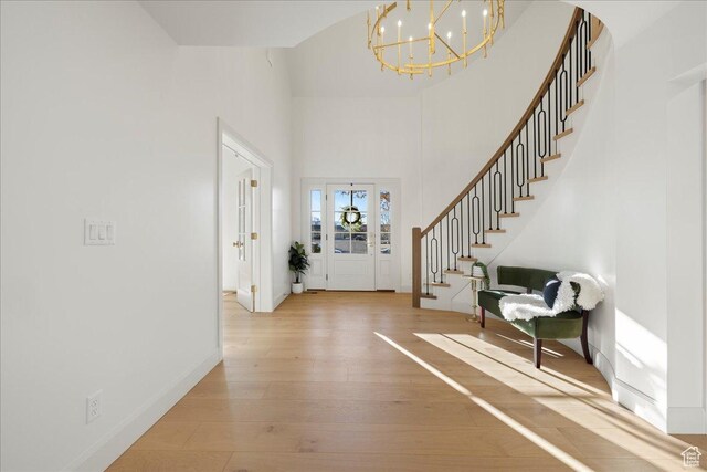 entrance foyer with a chandelier, stairway, light wood-style flooring, a towering ceiling, and baseboards