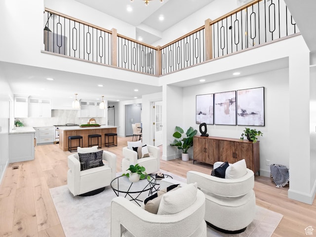 living area featuring light wood finished floors, baseboards, a high ceiling, and recessed lighting