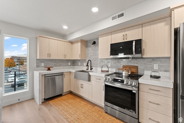 kitchen featuring appliances with stainless steel finishes, a sink, light brown cabinetry, light countertops, and recessed lighting