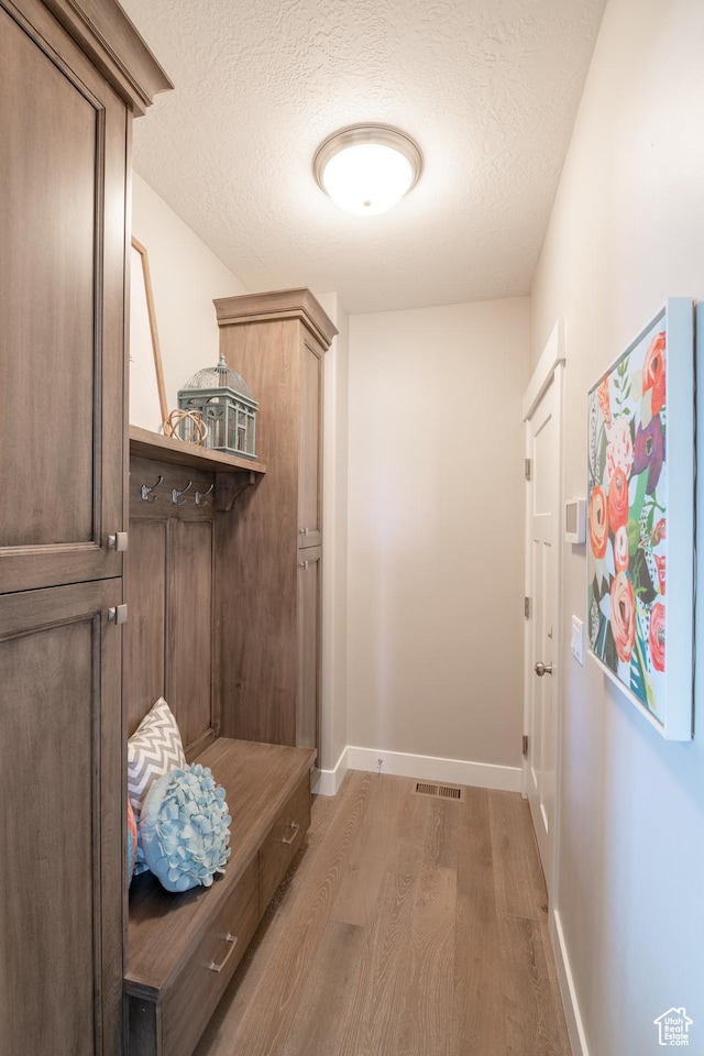 12751 S Harvest Ln W Unit 6, Riverton, UT 84096 - mudroom featuring light wood finished floors, baseboards, visible vents, and a textured ceiling