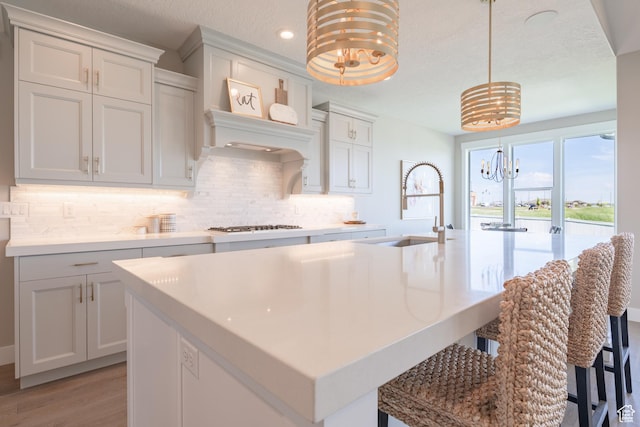 12751 S Harvest Ln W Unit 6, Riverton, UT 84096 - kitchen with light countertops, backsplash, a sink, a chandelier, and a kitchen island with sink