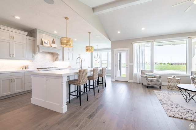 12751 S Harvest Ln W Unit 6, Riverton, UT 84096 - kitchen with vaulted ceiling, a kitchen bar, a center island with sink, light wood-style floors, and decorative backsplash