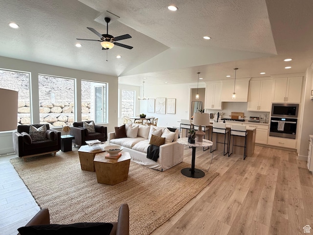 living area with recessed lighting, vaulted ceiling, light wood-style flooring, and a textured ceiling