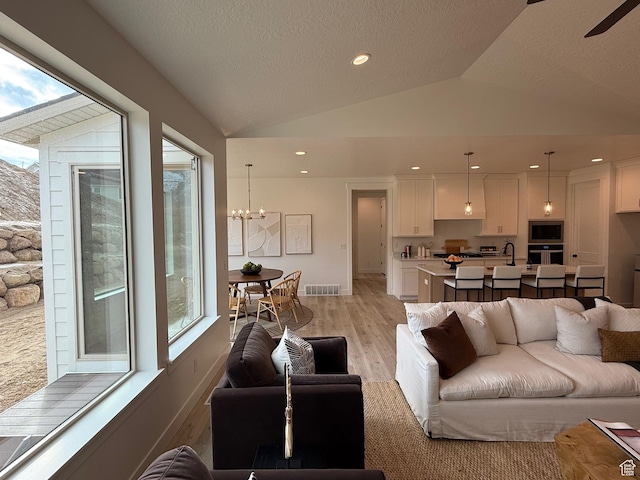living area featuring a textured ceiling, a notable chandelier, visible vents, vaulted ceiling, and light wood-type flooring