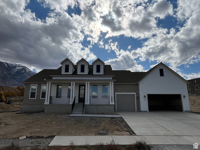 view of front facade featuring concrete driveway, an attached garage, covered porch, a mountain view, and brick siding