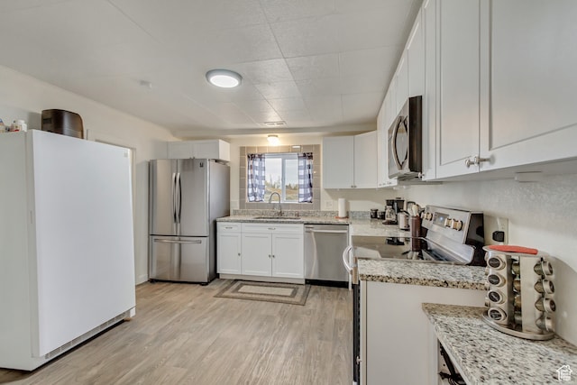 kitchen featuring light stone counters, white cabinets, sink, light wood-type flooring, and appliances with stainless steel finishes