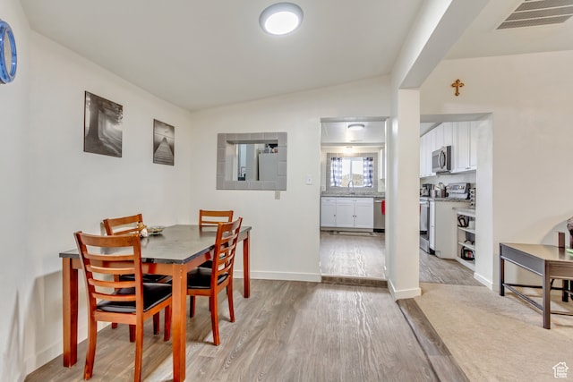 dining area featuring sink, light wood-type flooring, and lofted ceiling