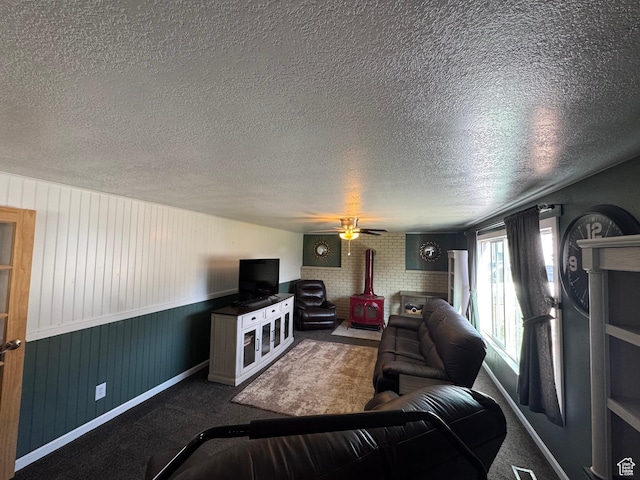carpeted living room with a wood stove, a textured ceiling, ceiling fan, and baseboards