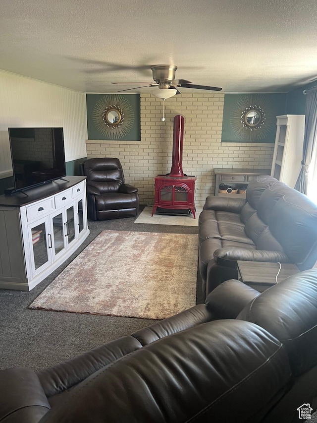 carpeted living room featuring a wood stove, a textured ceiling, a ceiling fan, and brick wall
