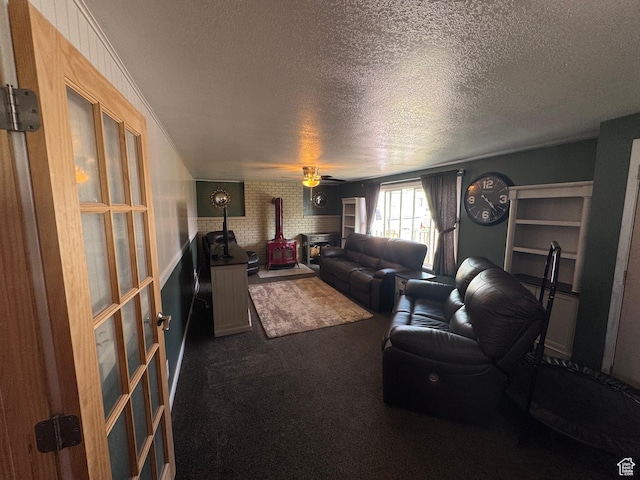 living room with dark colored carpet, a textured ceiling, a ceiling fan, and a wood stove