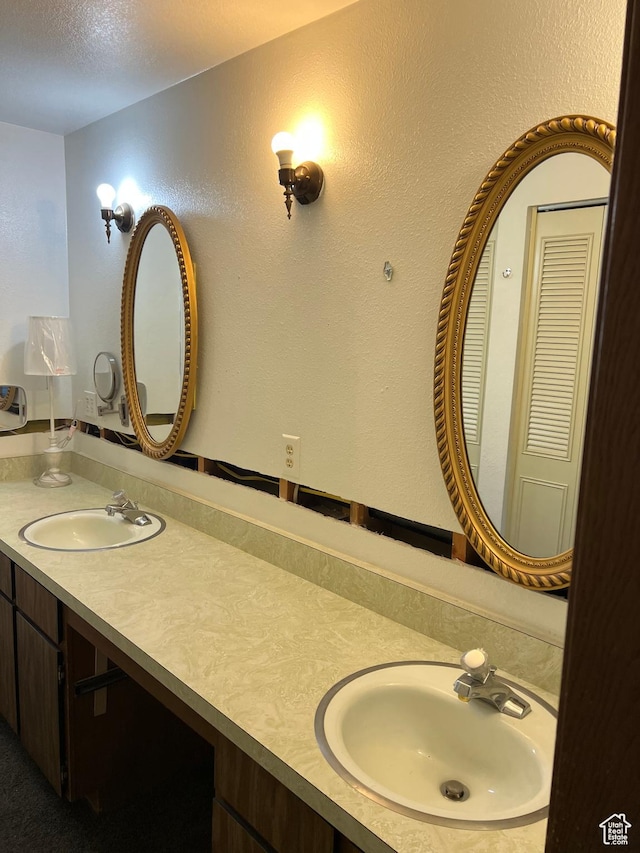 full bath with double vanity, a sink, and a textured ceiling
