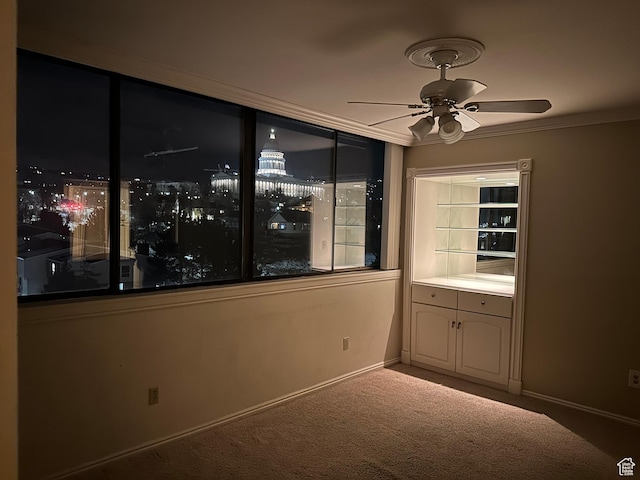 carpeted spare room with a ceiling fan, crown molding, and baseboards