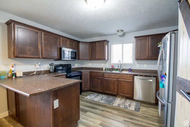 kitchen with kitchen peninsula, dark brown cabinets, stainless steel appliances, and light hardwood / wood-style floors