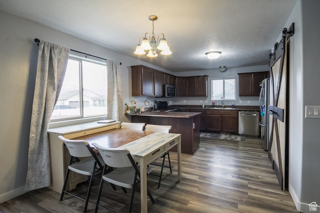 kitchen with a barn door, dark wood-type flooring, decorative light fixtures, and appliances with stainless steel finishes